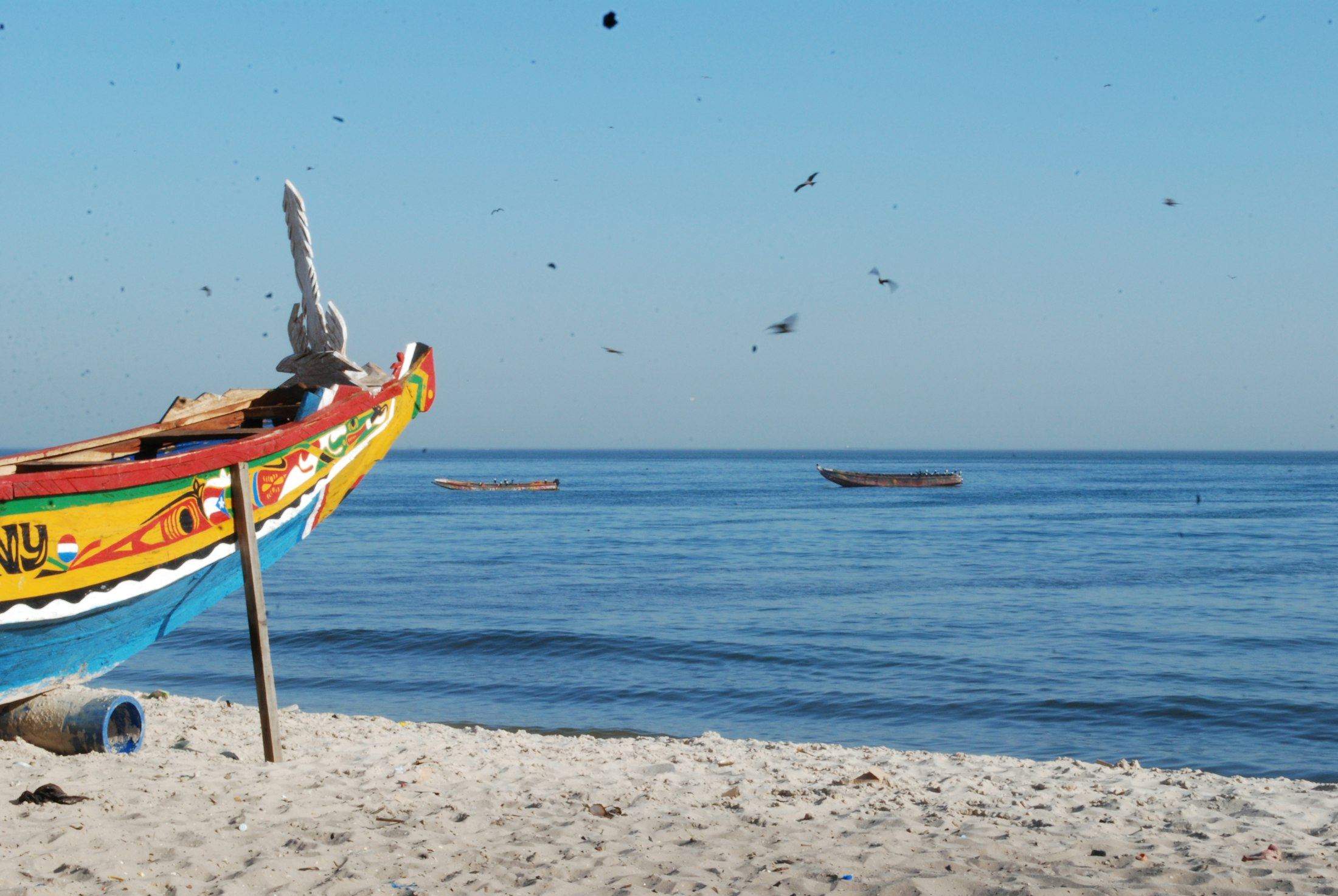 Une pirogue peinte de couleurs vives posée sur le sable, face à l’océan bleu.